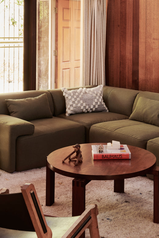 Living room with brown sectional sofa, round wooden coffee table, and decorative items.